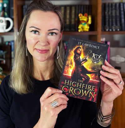 JT Lawrence, USA Today bestselling urban fantasy author, holding a paperback of The HighFire Crown (Blood Magic Book 1)